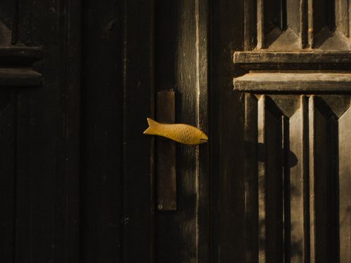 Free A close-up view of a vintage wooden door featuring a unique yellow fish-shaped handle in Gdynia, Poland. Stock Photo