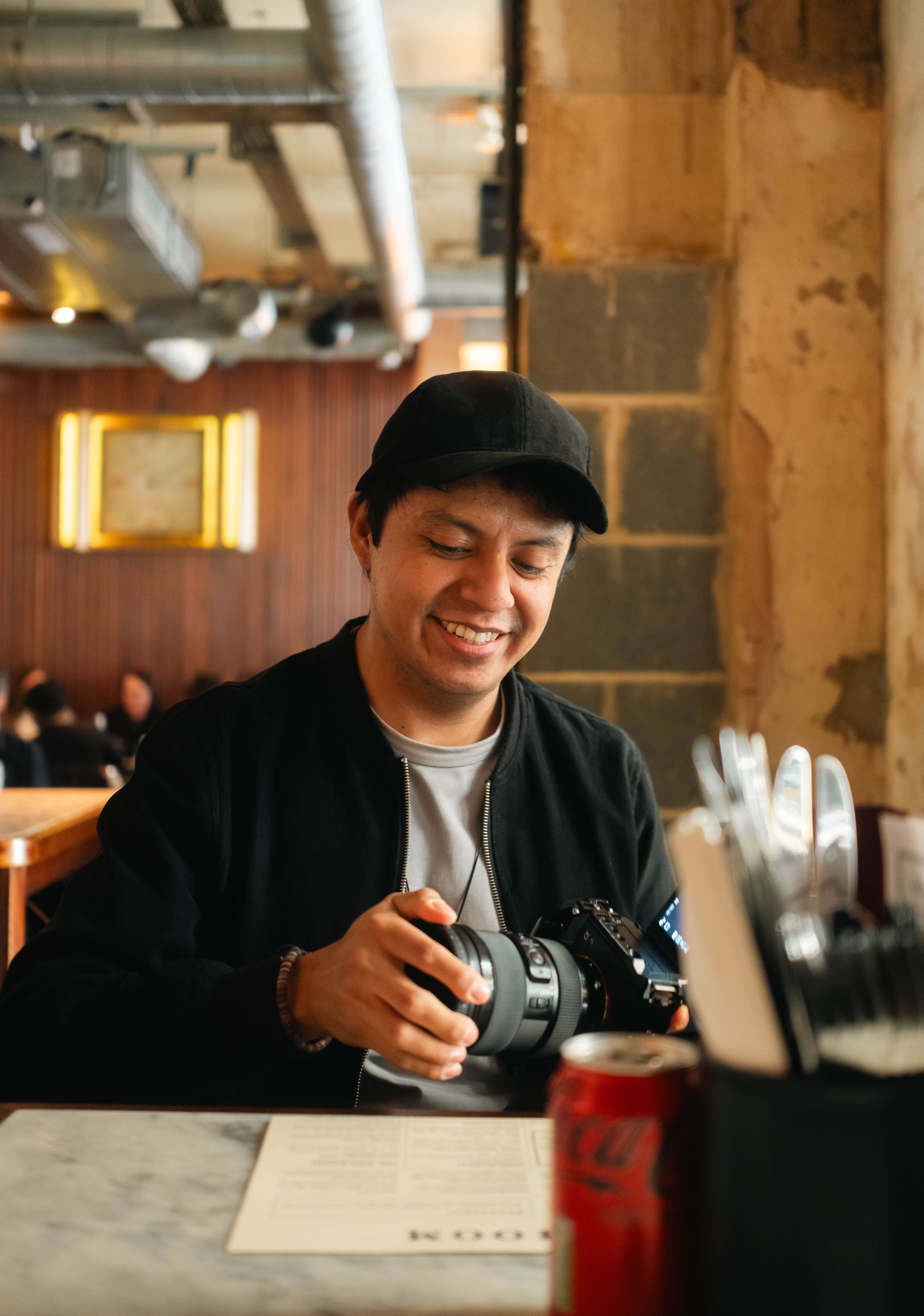 An adult man smiling while examining his camera in a relaxed cafe setting, captured indoors.