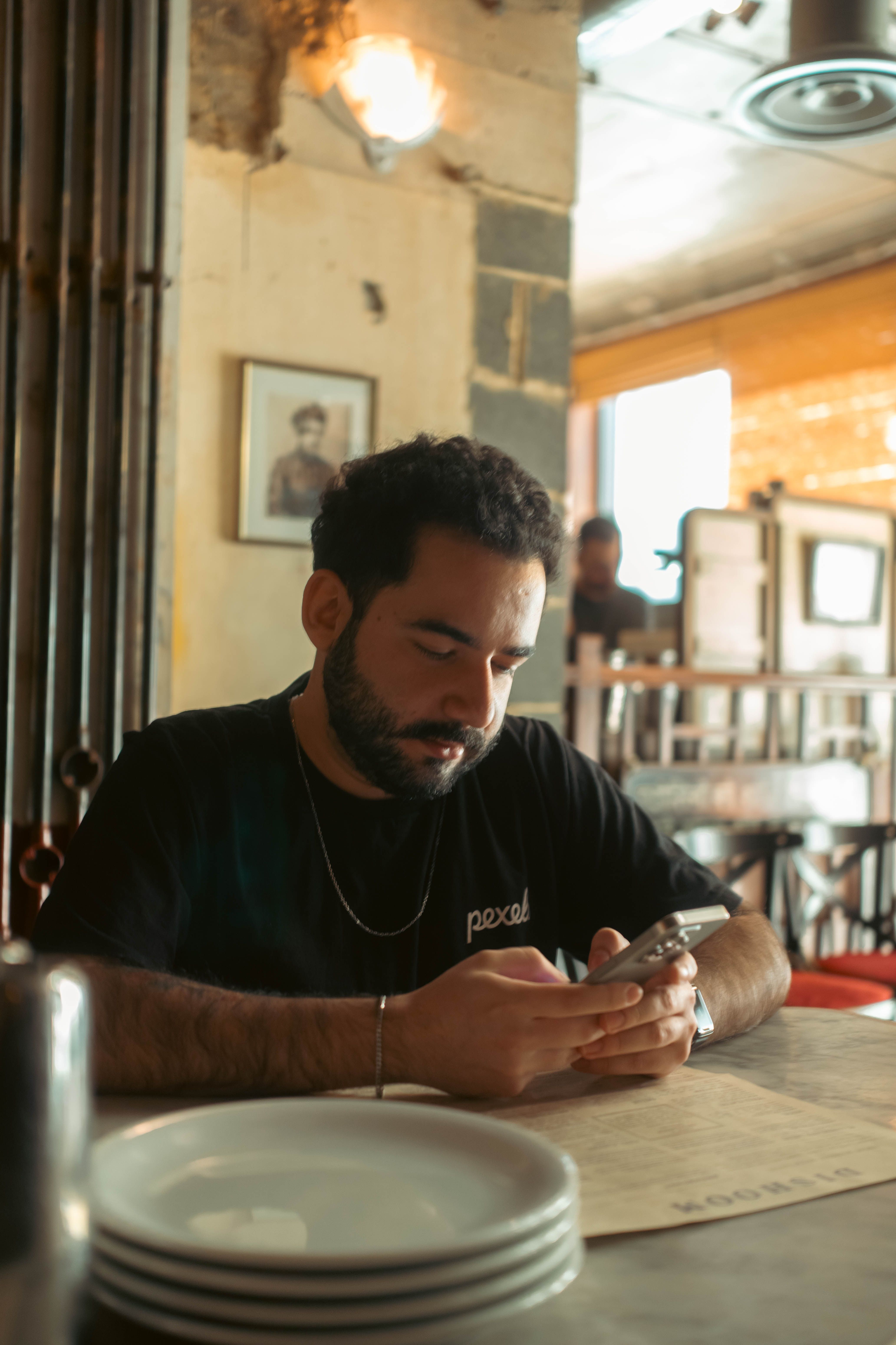 Young man sitting at a café table using his smartphone, surrounded by a warm, rustic ambiance.