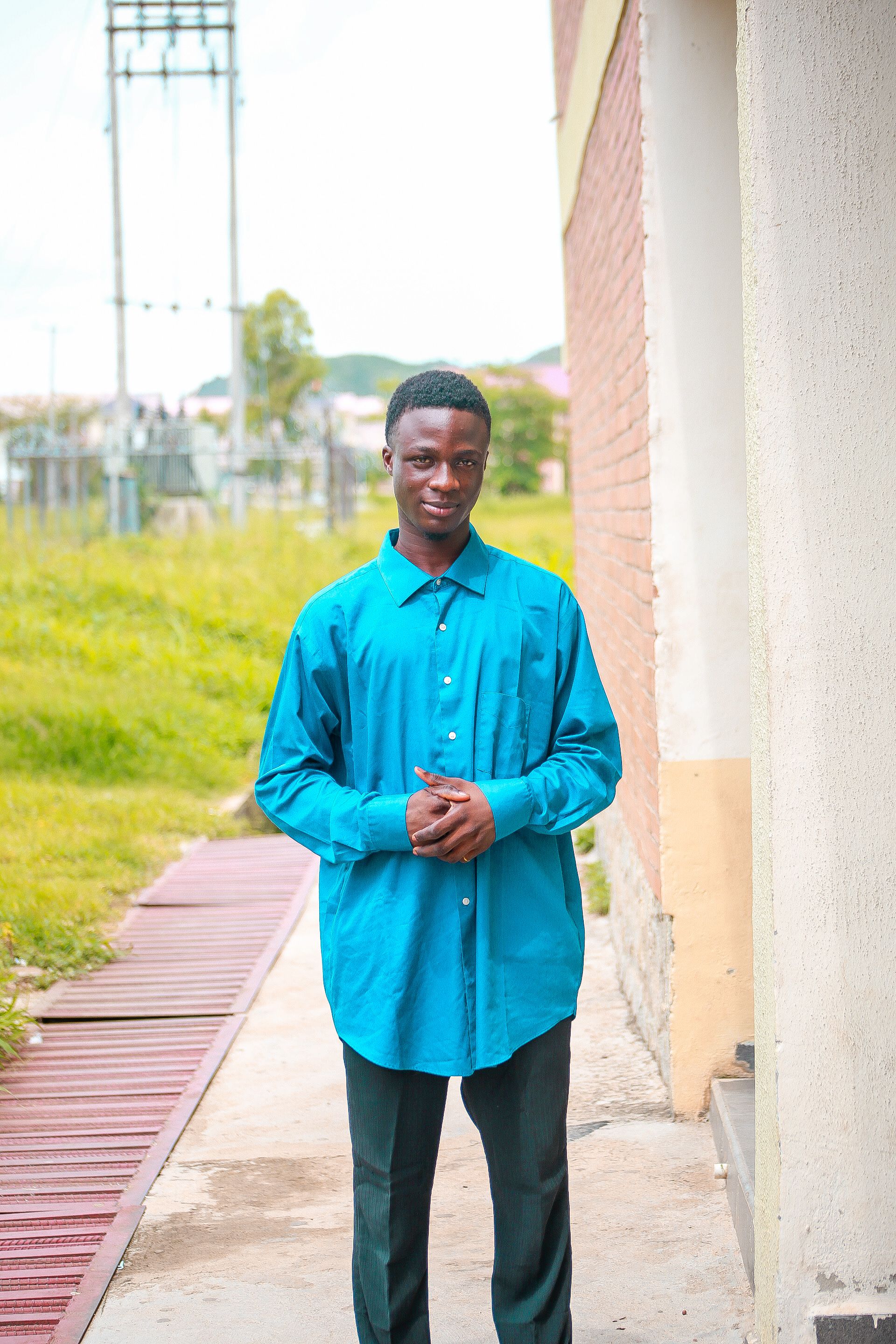 A young man in a blue shirt smiles confidently while standing outdoors.