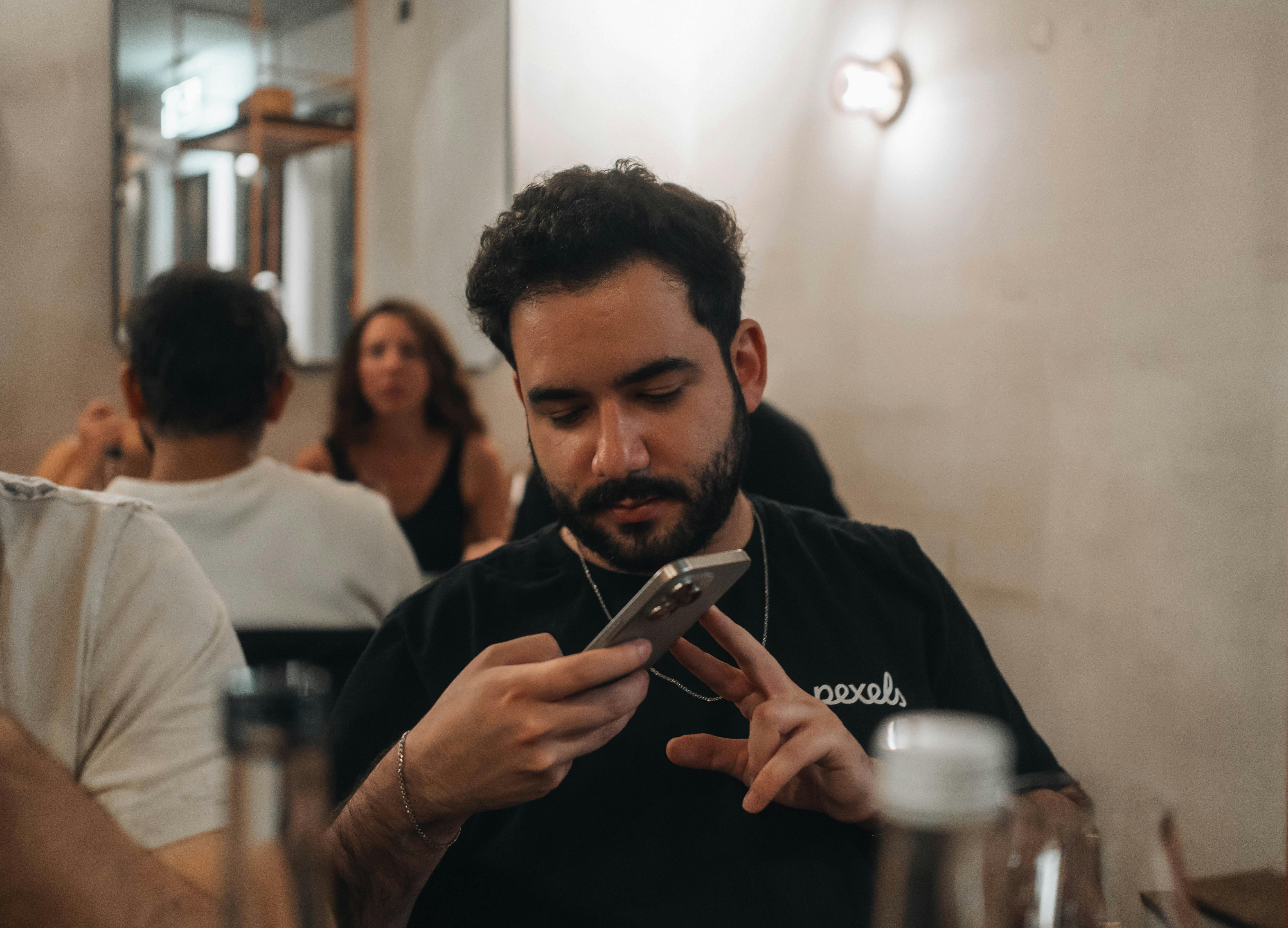 Gratuit Tânăr se concentrează pe smartphone într-o cafenea confortabilă, făcând multitasking cu ajutorul tehnologiei. Fotografie de stoc