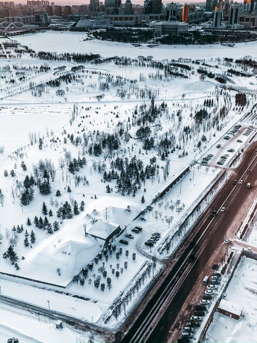 Free A stunning aerial view of a snowy landscape with roads and trees in an urban area during winter. Stock Photo