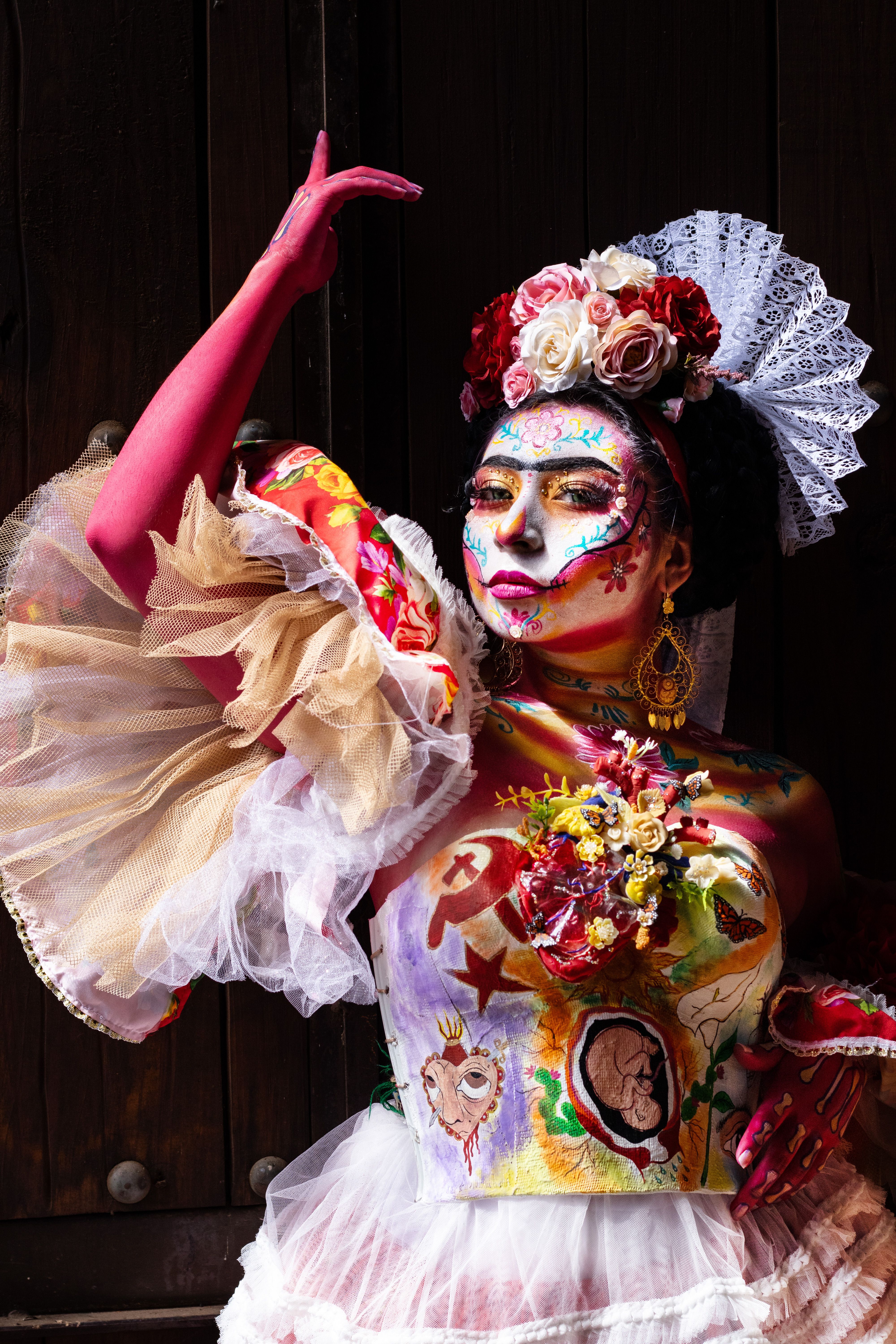 Vibrant body art portrait of a woman with floral headpiece and painted face.