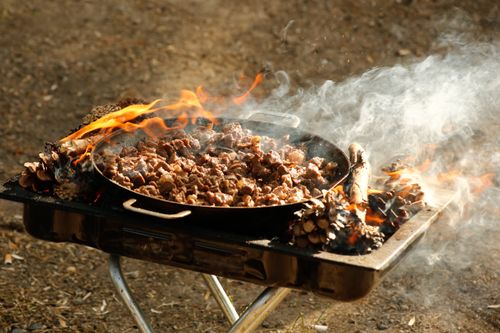 Free Close-up of sizzling meat cooking on an outdoor barbecue grill surrounded by flames and smoke. Stock Photo