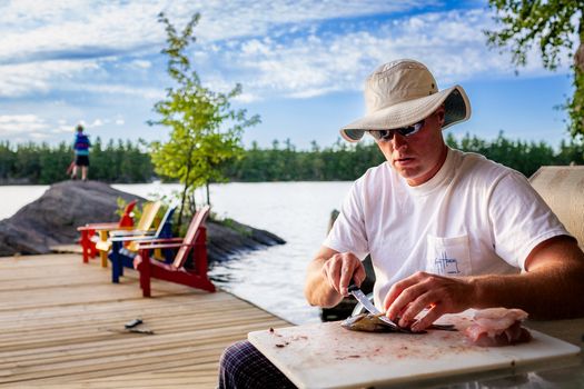 Man cleaning fish on a dock by Buck Lake with vibrant summer scenery.