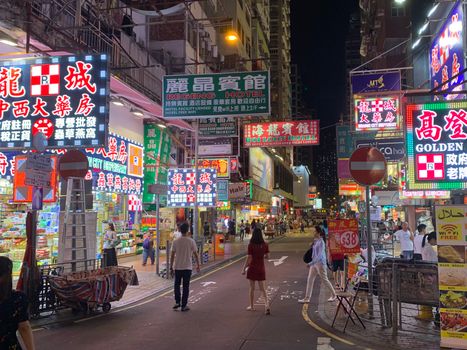 Lively night street in Hong Kong with bustling shops and neon signs.