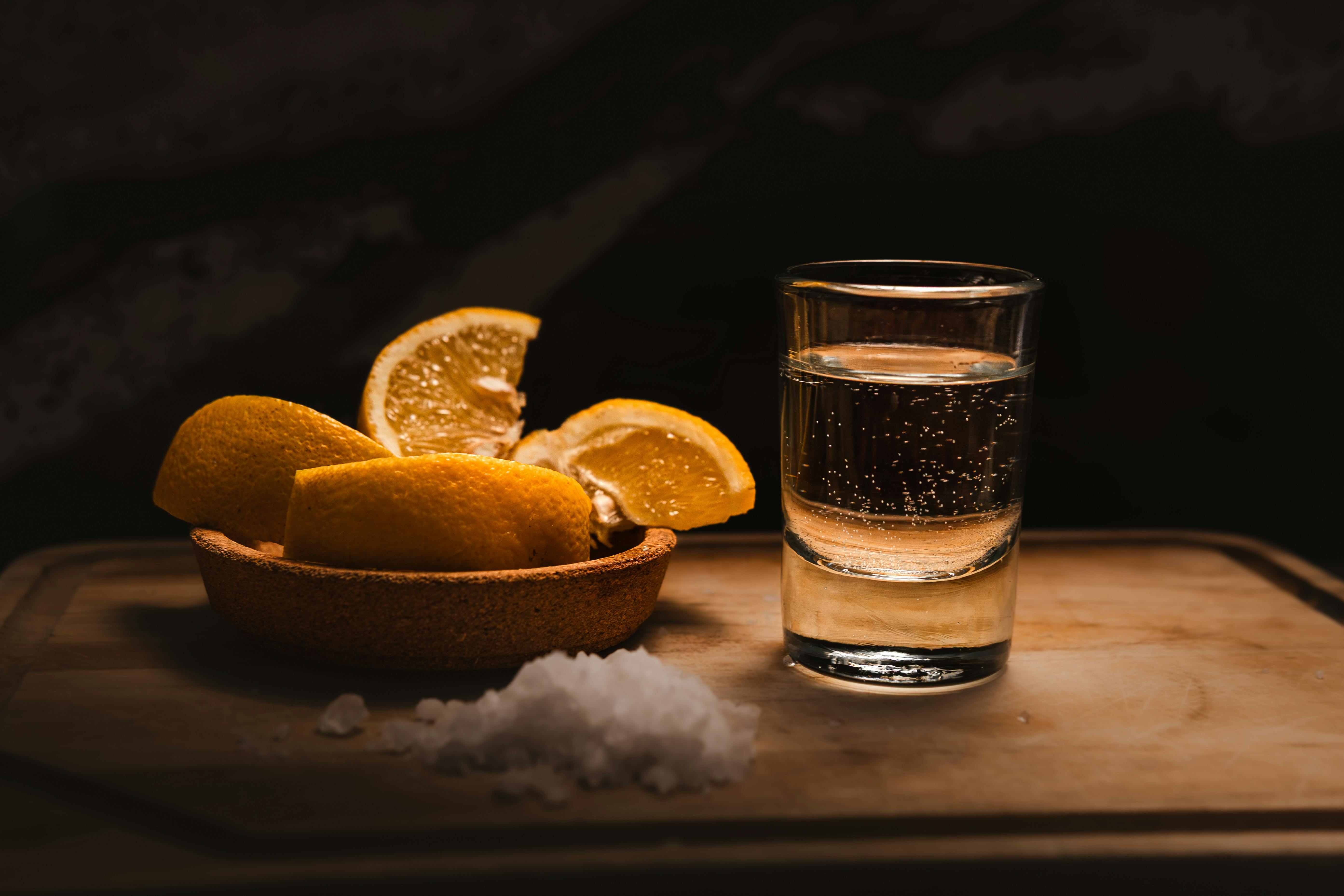 A vibrant tequila shot with lemon slices and salt on a bar counter under warm lighting.