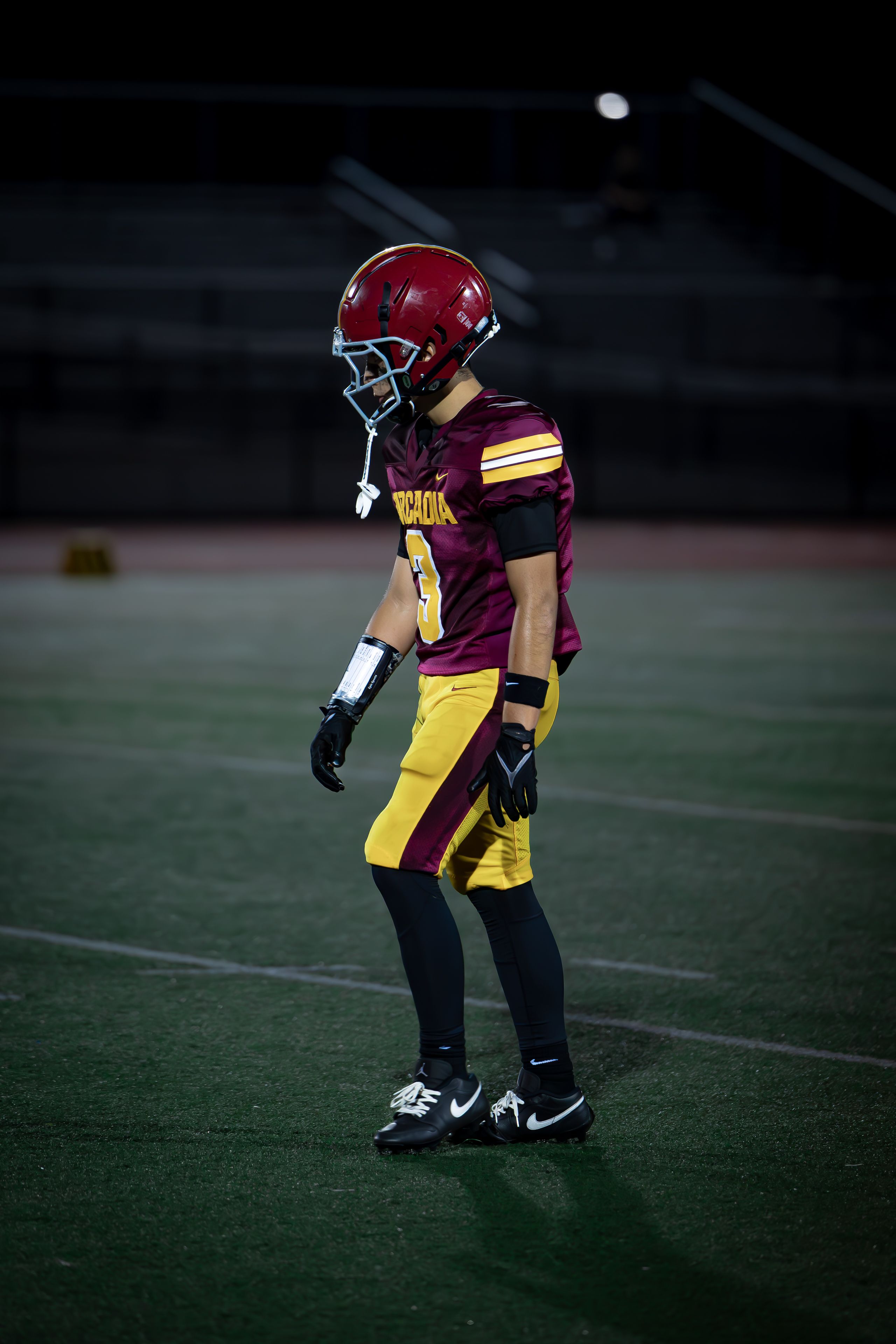 Focused athlete in full gear on a floodlit football field, exuding determination.