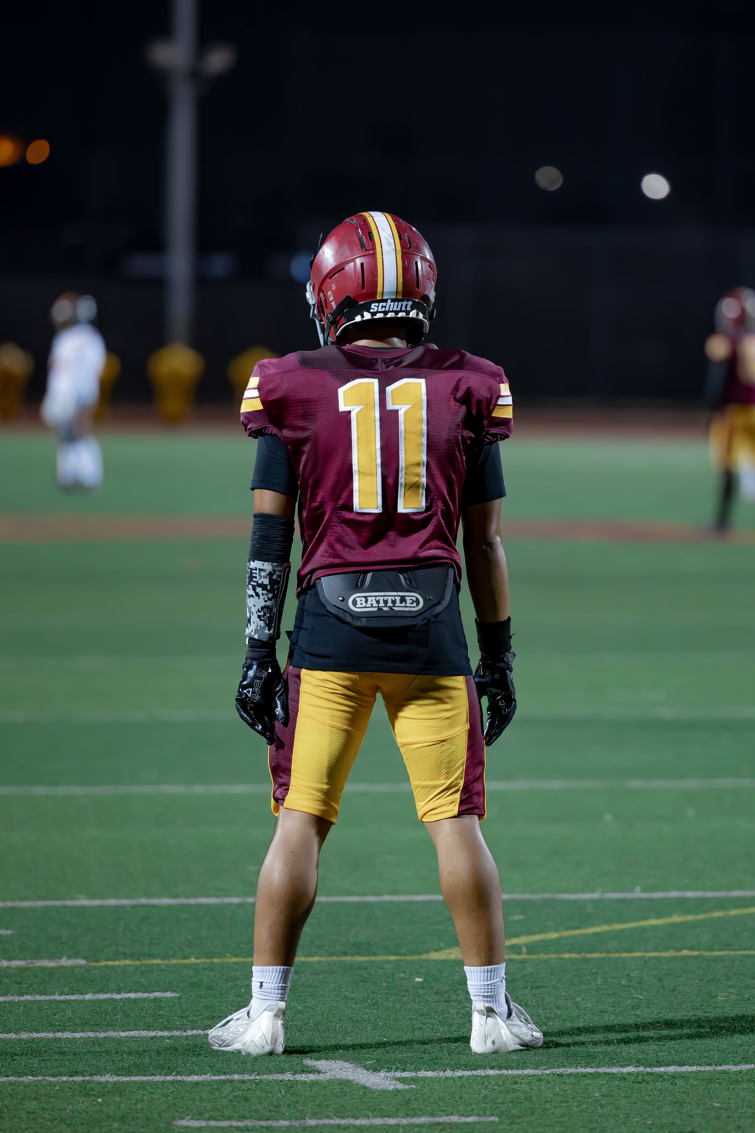 Football player in gear during a high school night game. Focused on the field.