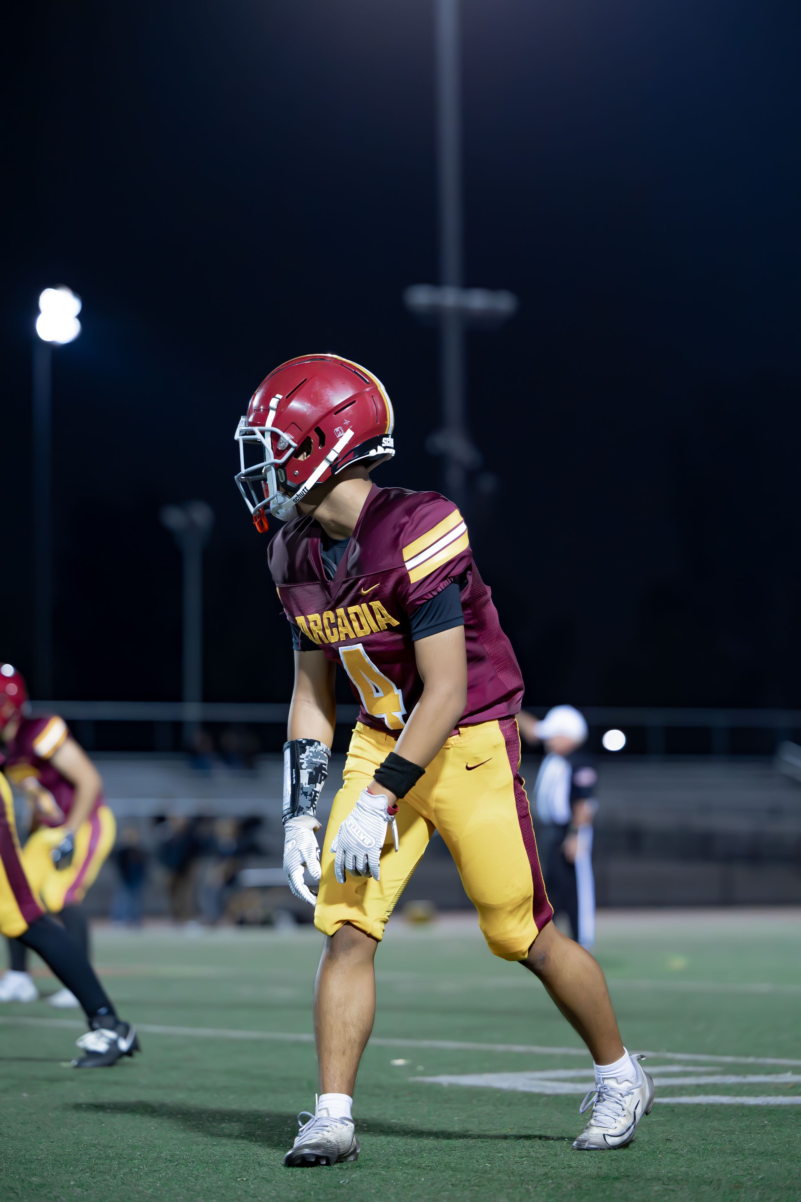 Focused high school football player in uniform on a night game under stadium lights.