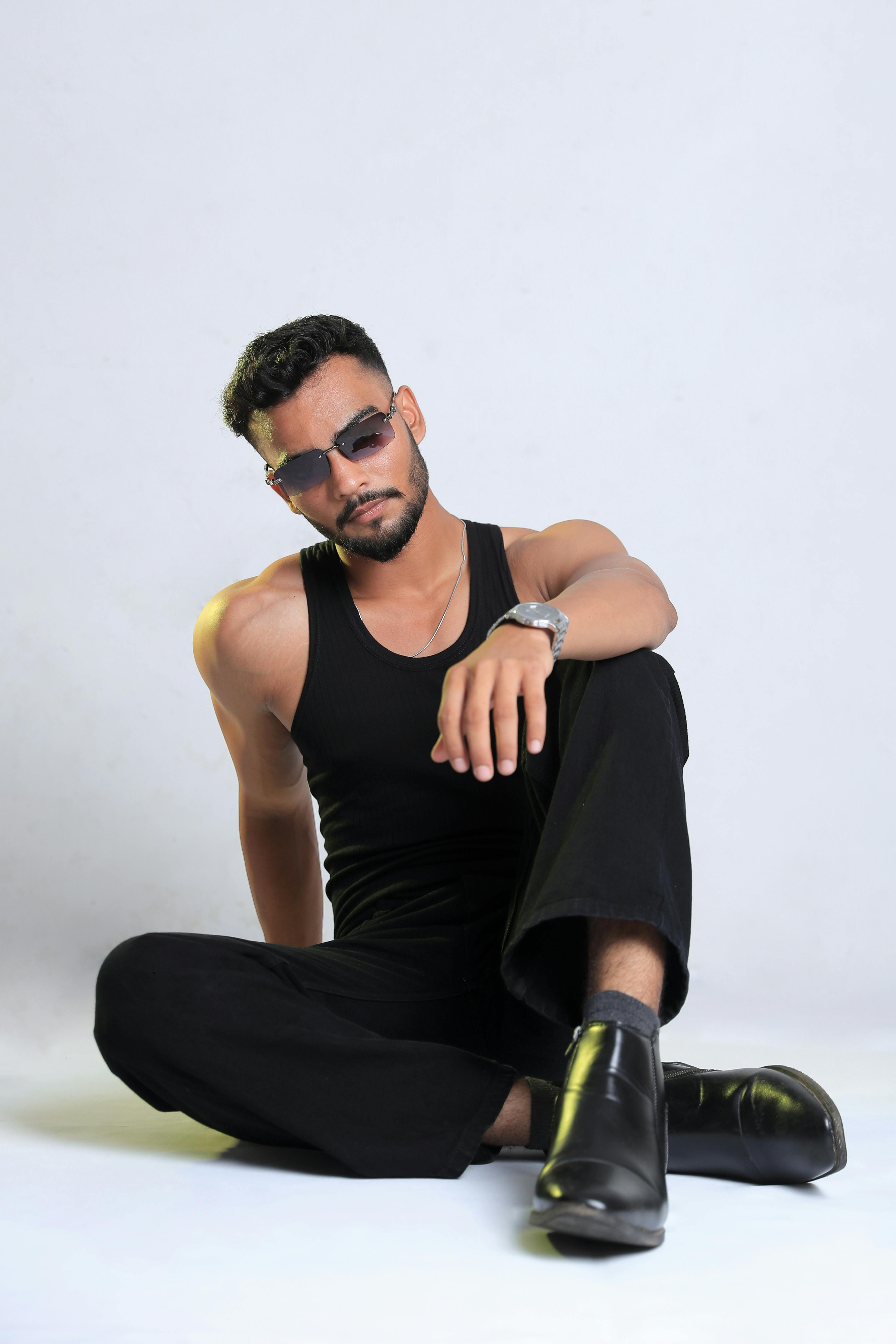 Stylish man in black outfit posing against a minimalist white background.