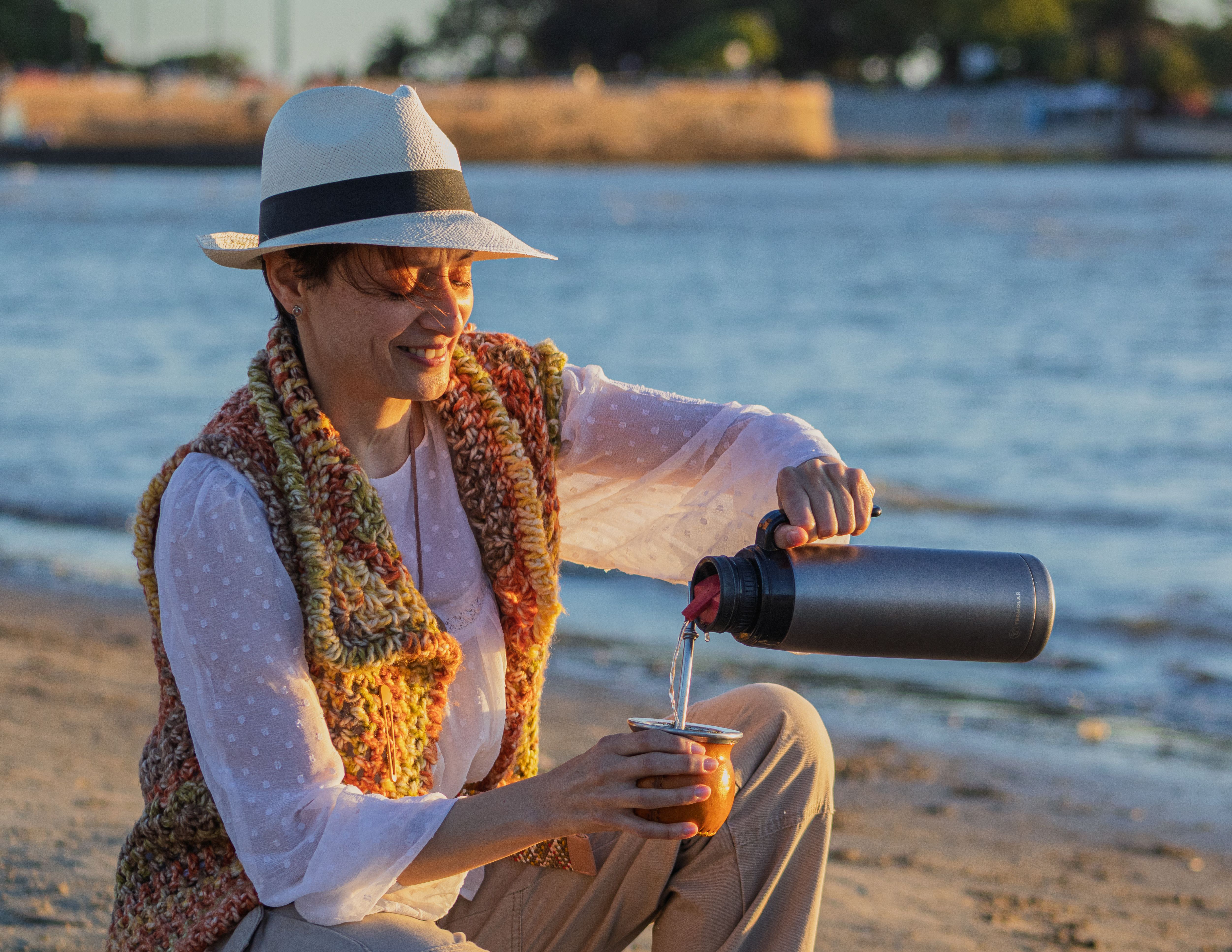 Adult woman pours yerba mate on Montevideo beach, Uruguay, at sunset.