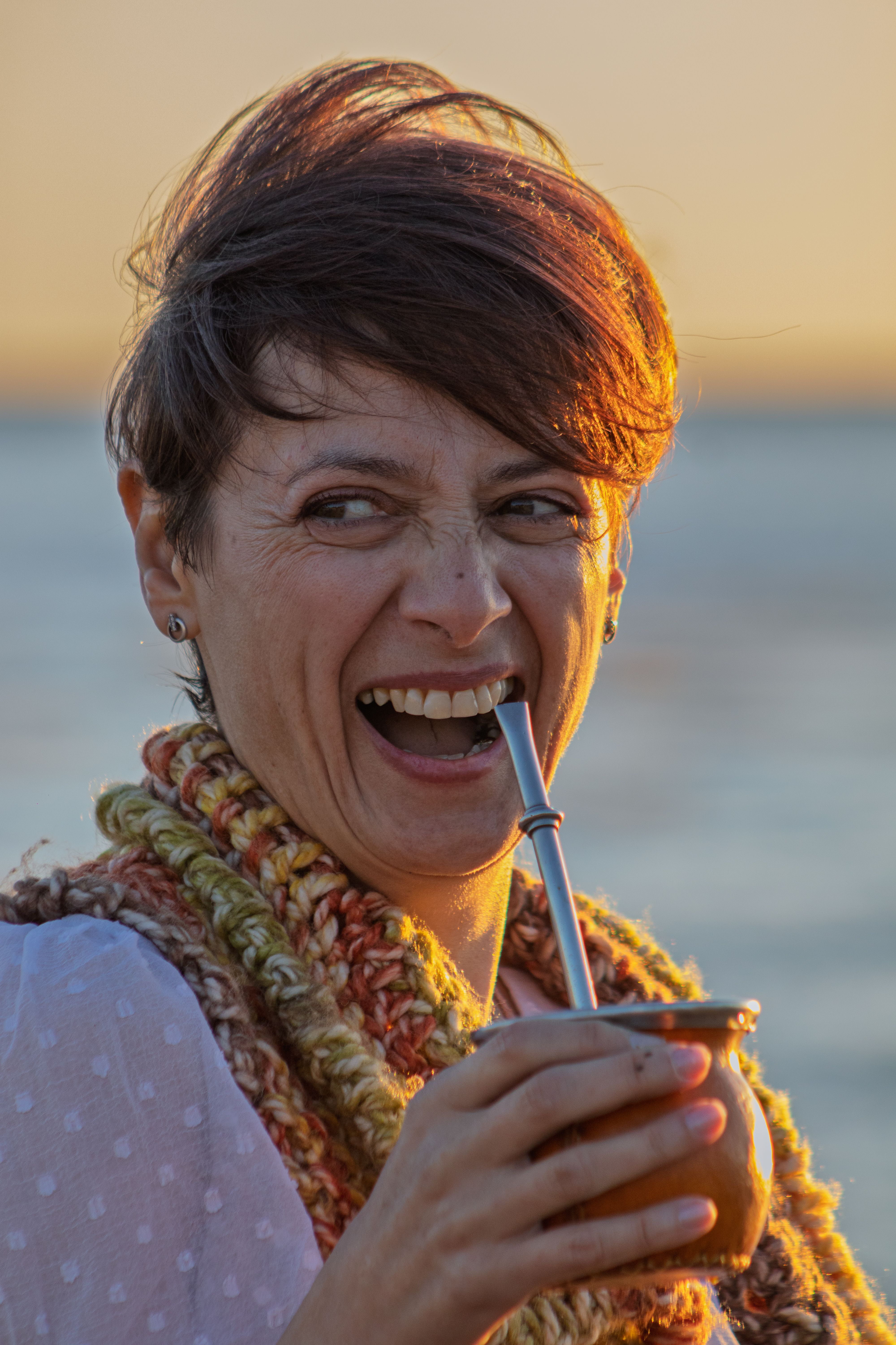 A joyful woman at Montevideo beach enjoying yerba mate during sunset, capturing the warmth of Uruguay's tradition.