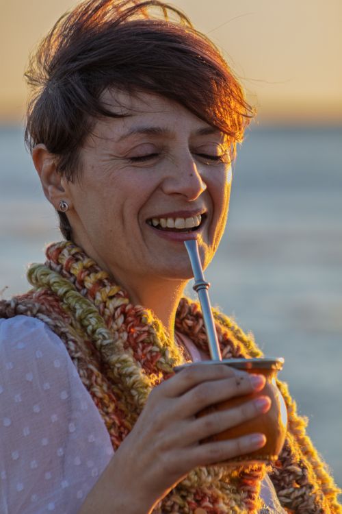 Free A joyful adult woman enjoys yerba mate at sunset on a Montevideo beach, Uruguay. Stock Photo