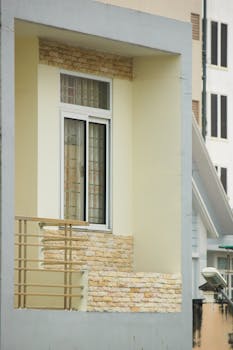 Contemporary balcony design featuring stone wall and glass window in urban setting.