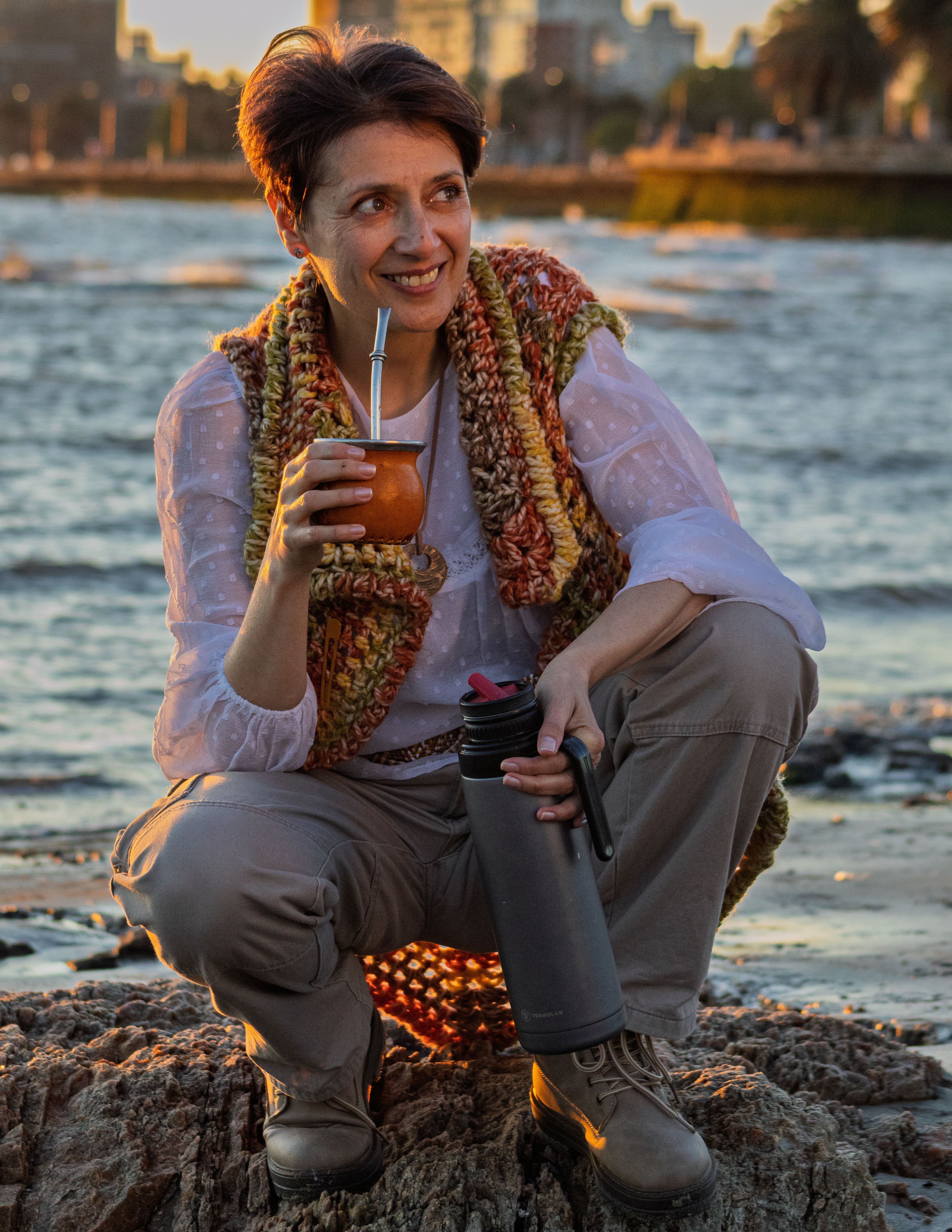 Adult woman savoring yerba mate on a rocky Montevideo beach at sunset.