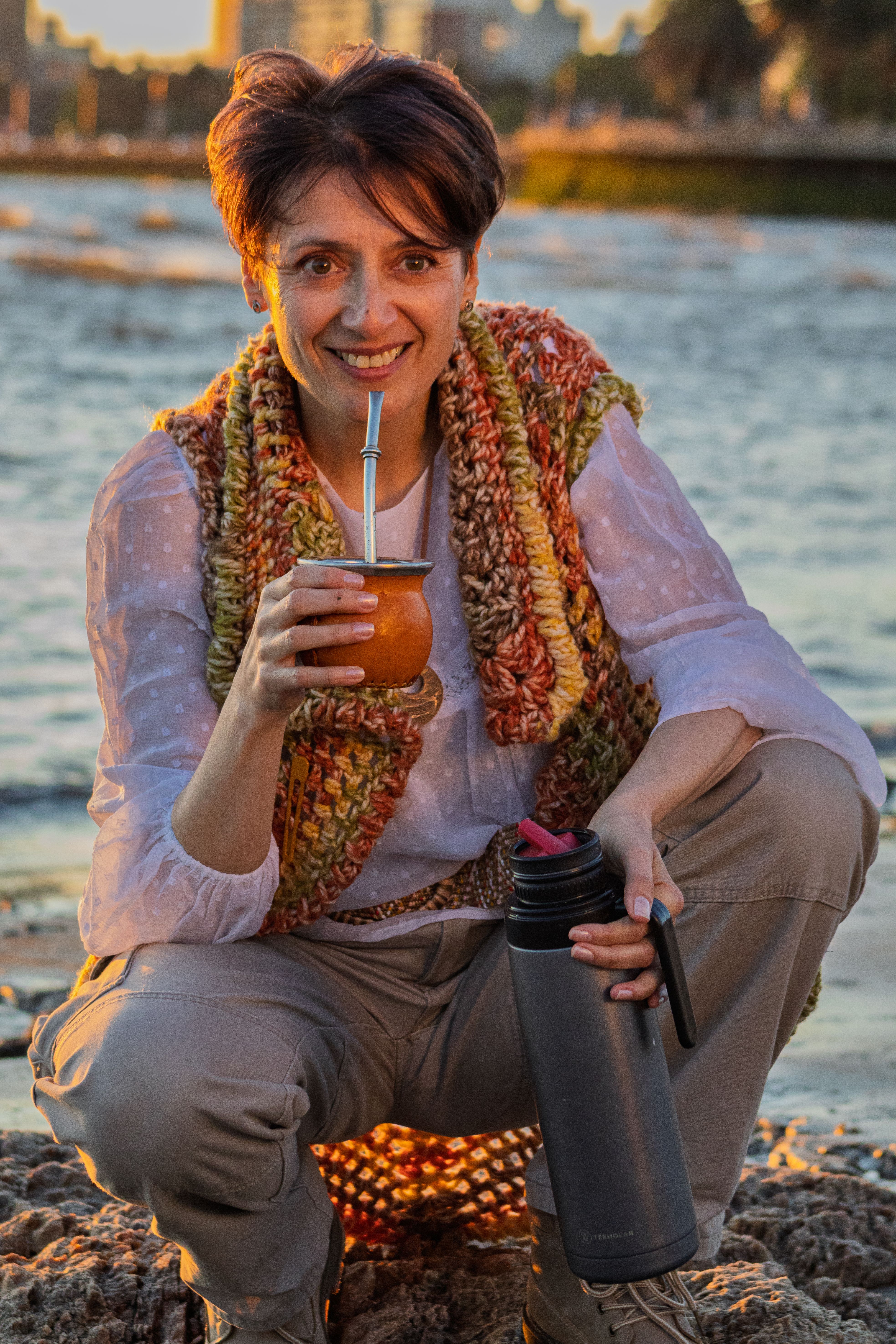 Woman enjoying traditional yerba mate on Montevideo beach during sunset, embodying relaxation and cultural heritage.