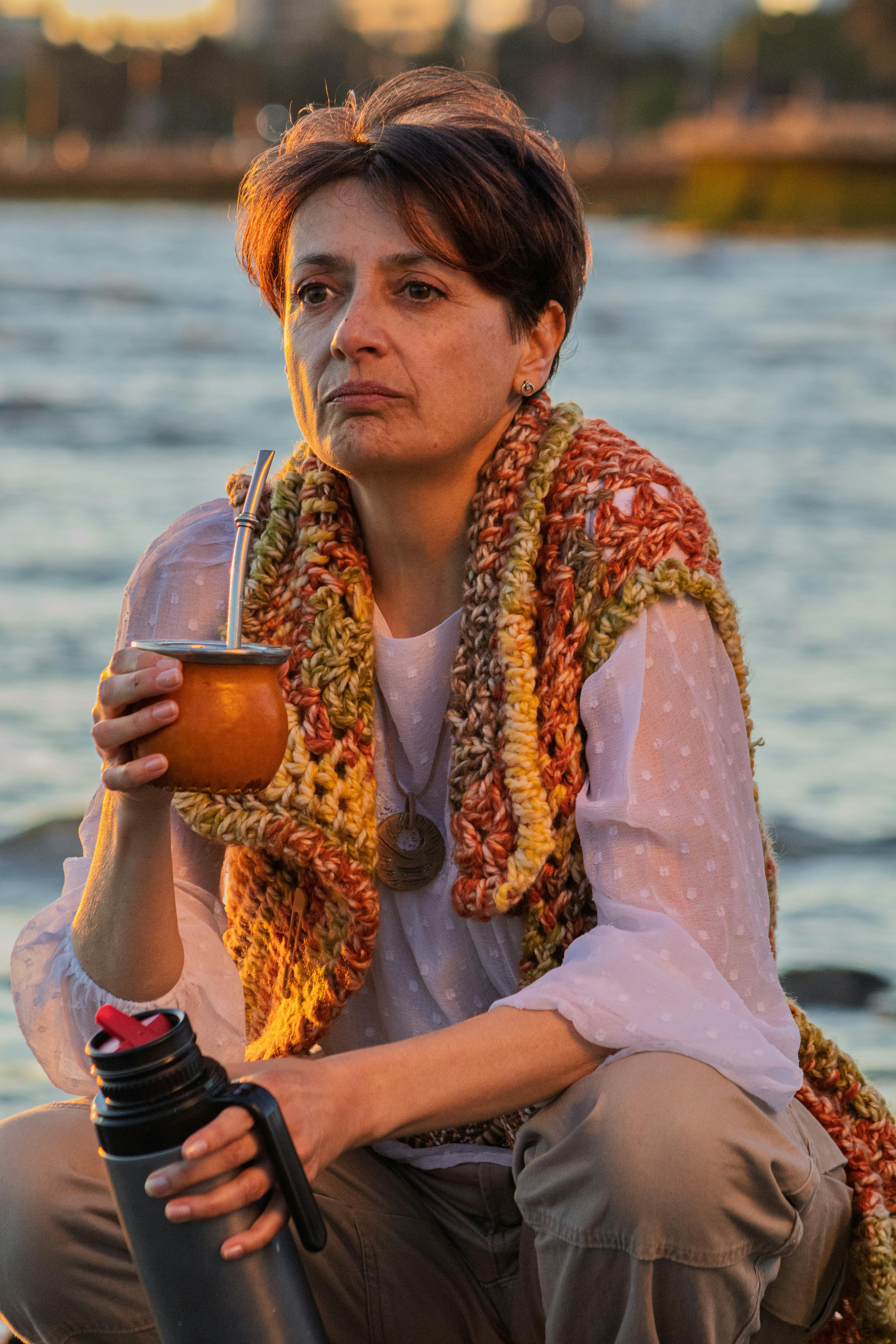 An adult woman at Montevideo beach enjoying yerba mate as the sun sets.