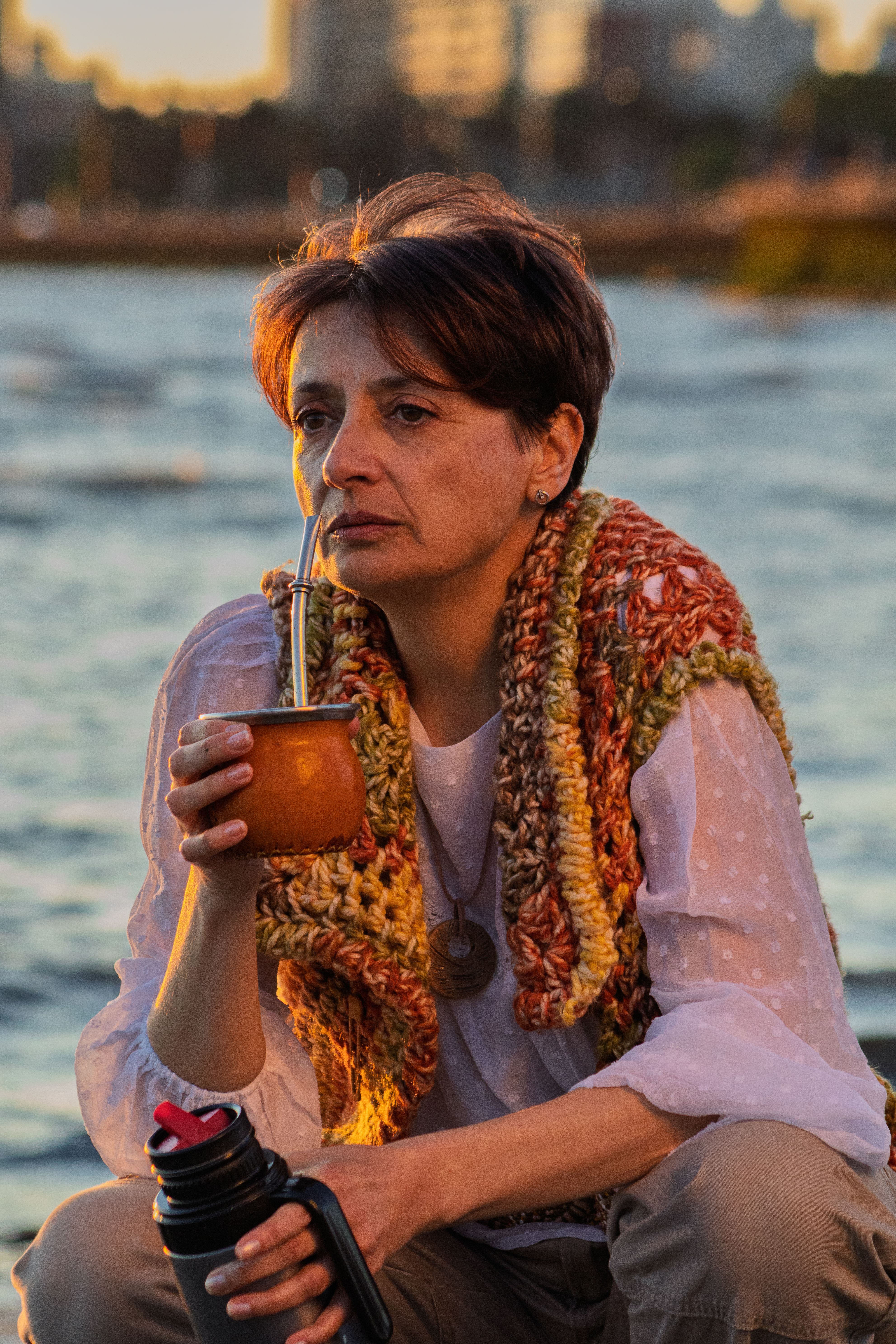 Adult woman savoring traditional yerba mate by the beach during a picturesque Montevideo sunset.