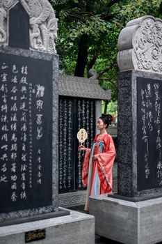 A woman in traditional attire admires inscriptions on stone tablets in a serene outdoor setting.