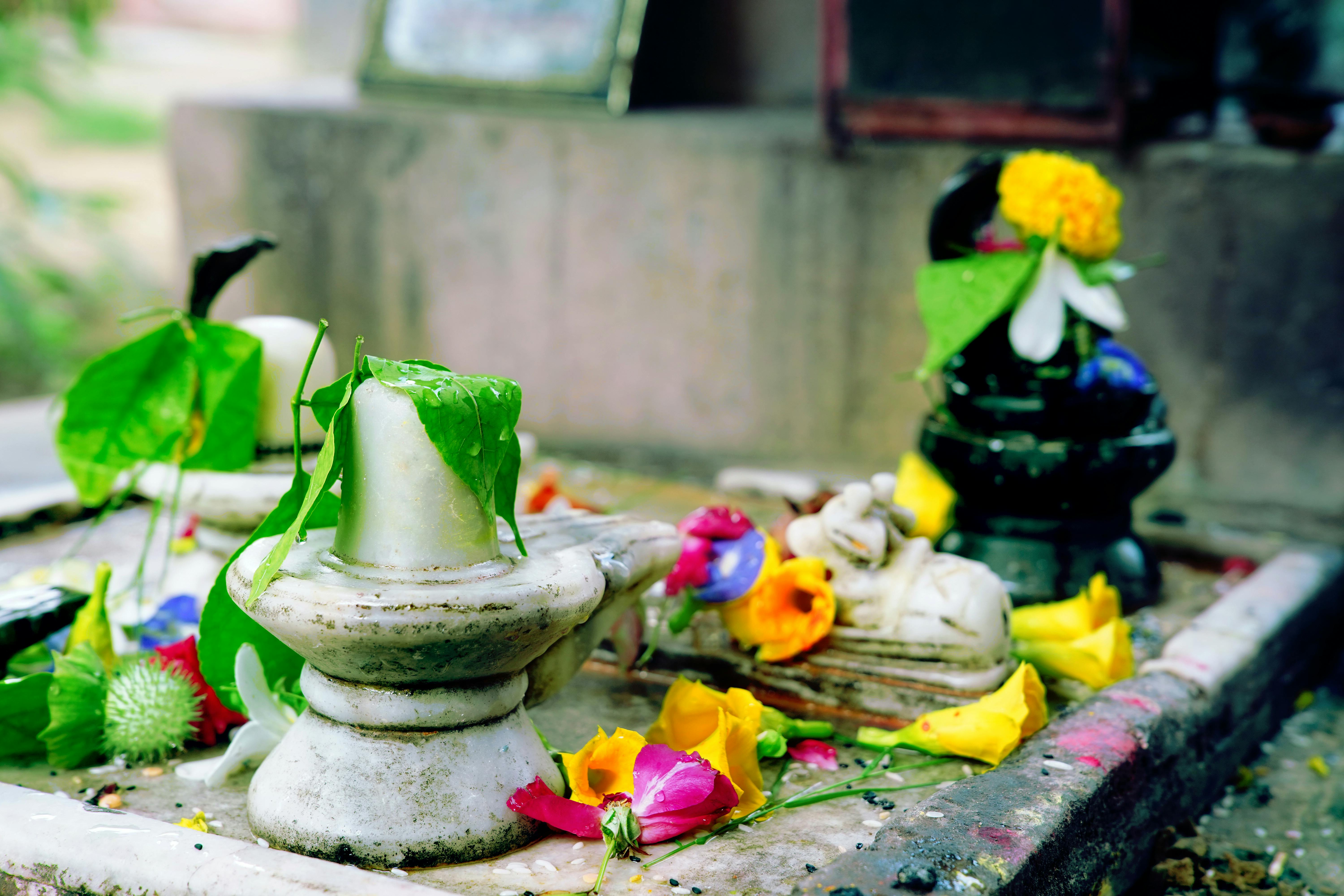 A colorful arrangement of flowers and leaves on Shiva lingam at an outdoor temple in India.