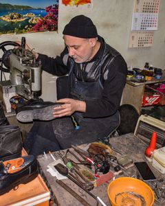 A cobbler meticulously repairs leather shoes in a traditional workshop setting.