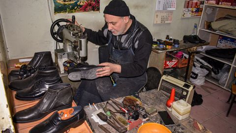 A cobbler meticulously repairs leather shoes in a traditional workshop setting.