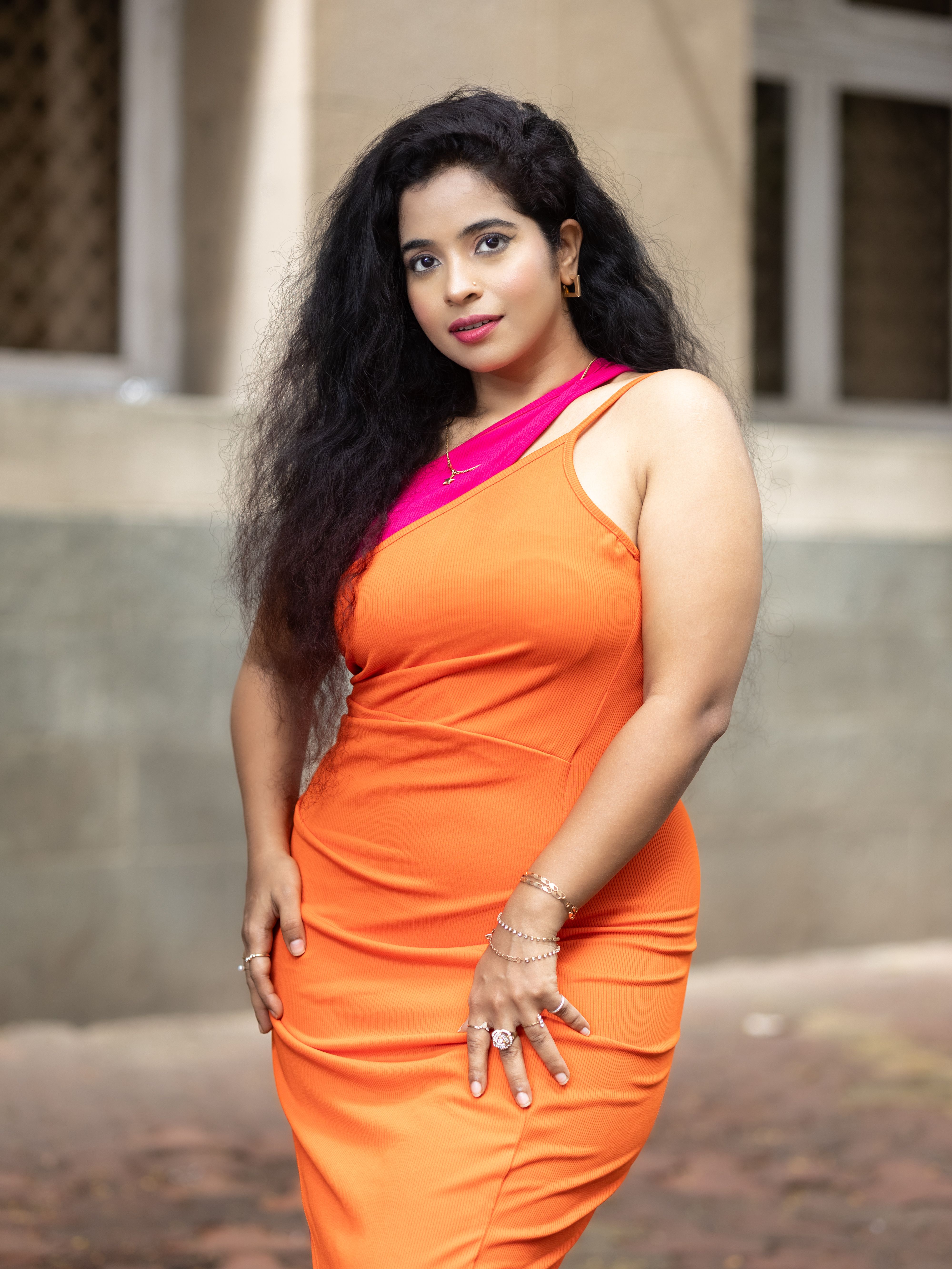 Confident woman posing in a vibrant orange dress outdoors, exuding style and elegance.