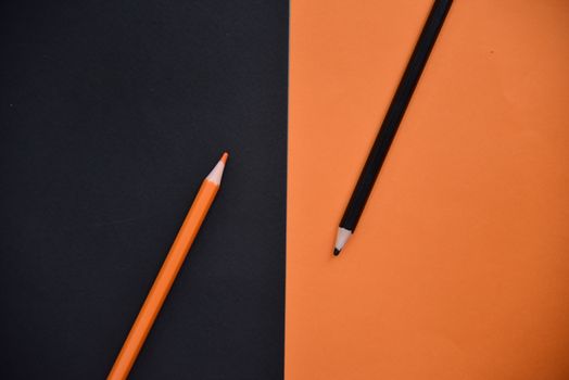 An artistic flat lay of orange and black pencils on orange and black background.