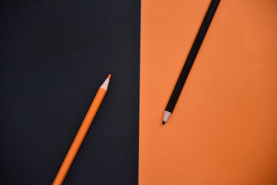 An artistic flat lay of orange and black pencils on orange and black background.