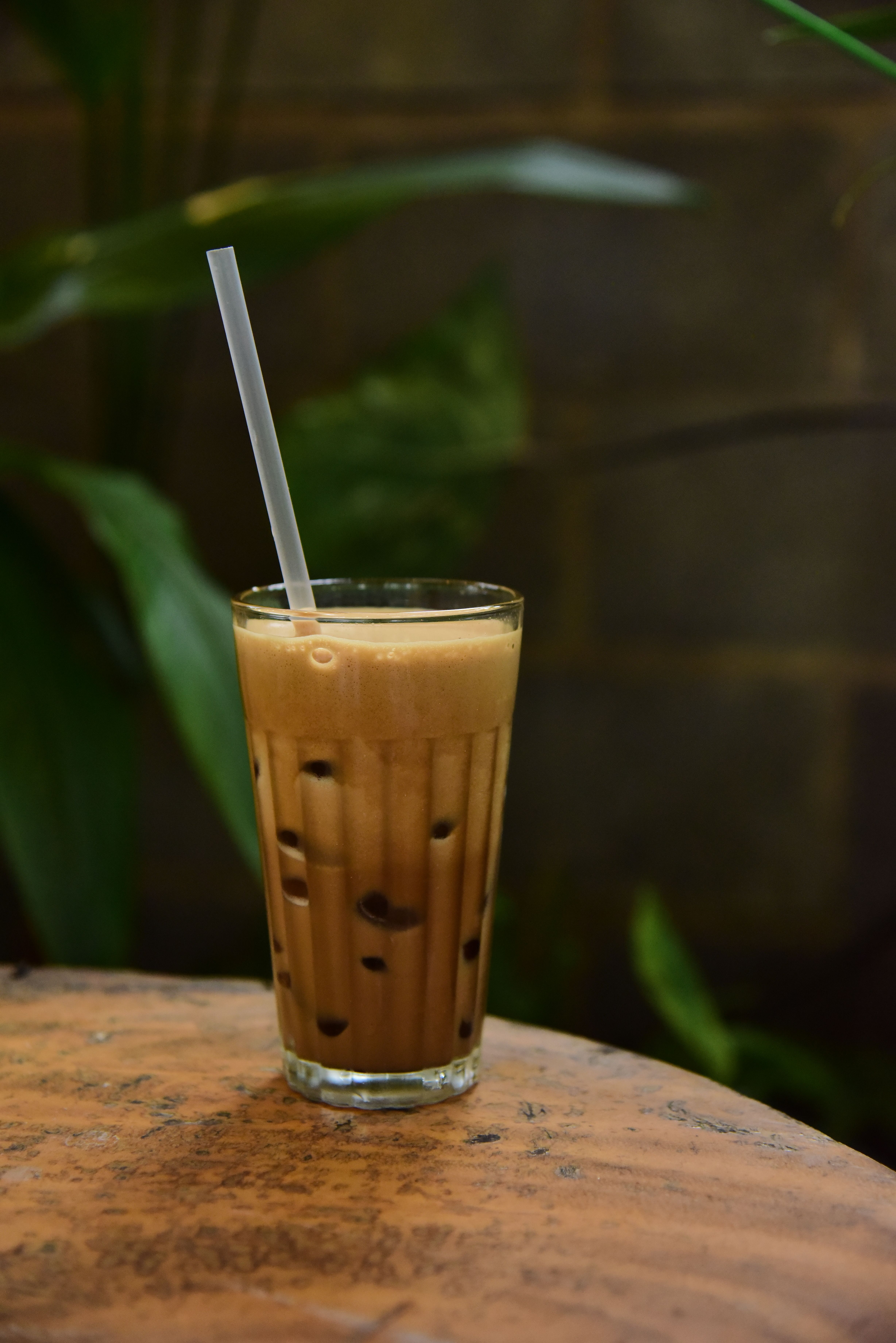 Verre strié de thé glacé aux perles de tapioca visibles, avec une paille, fond de feuillage flou