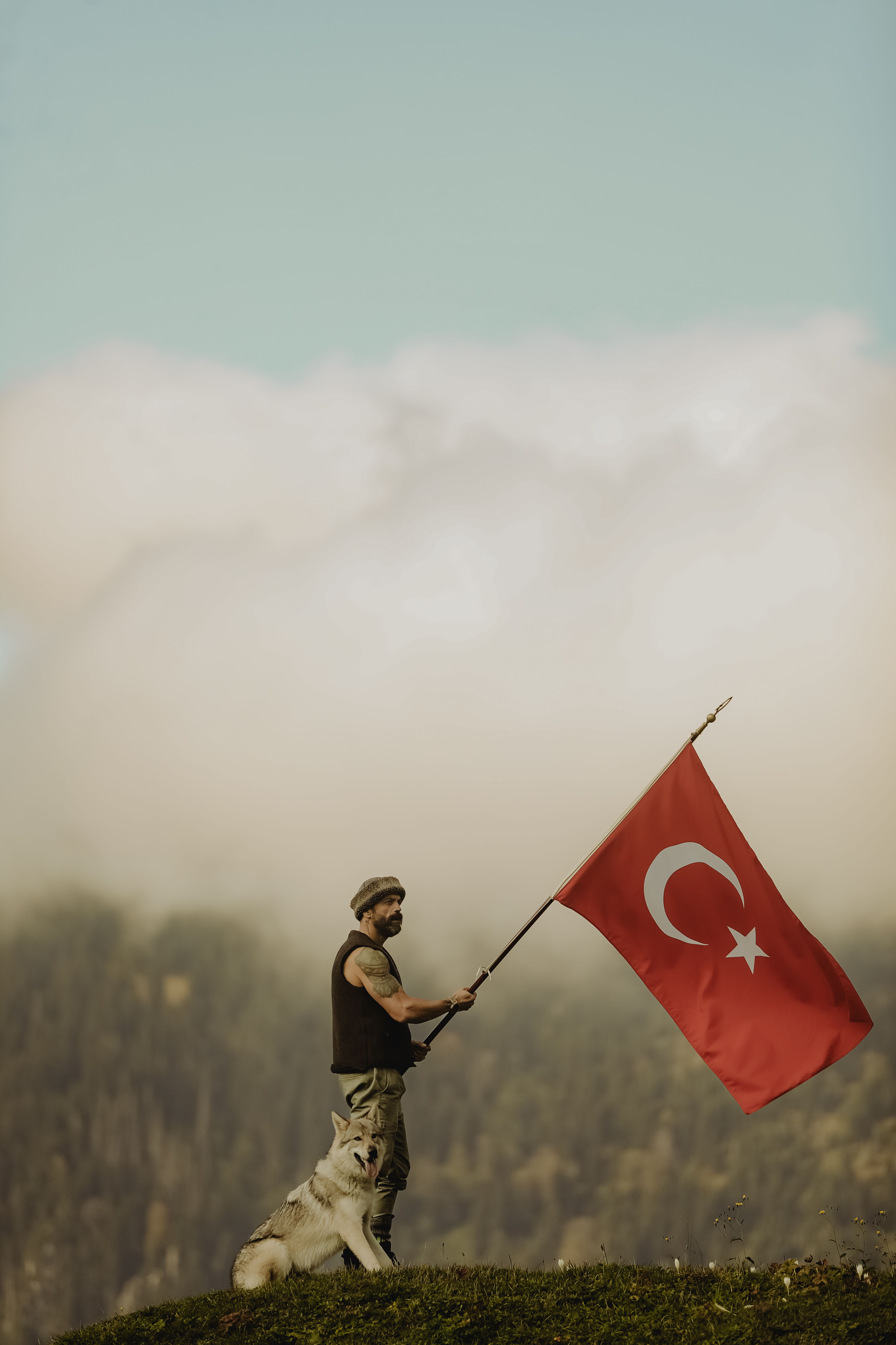 Man holding Turkish flag with mountain scenery and dog companion.