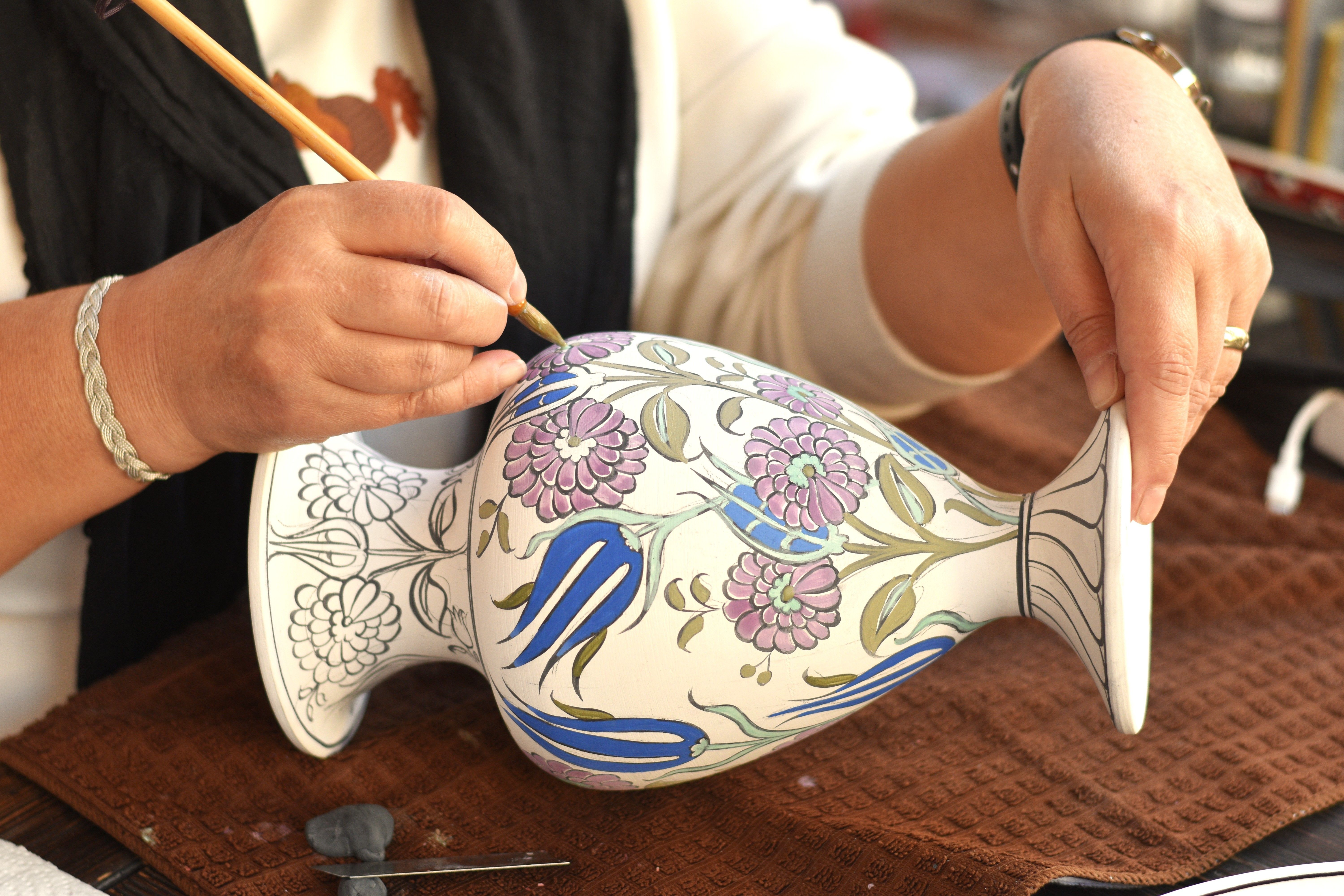 Close-up of an artisan hand-painting a delicate floral pattern on ceramic.