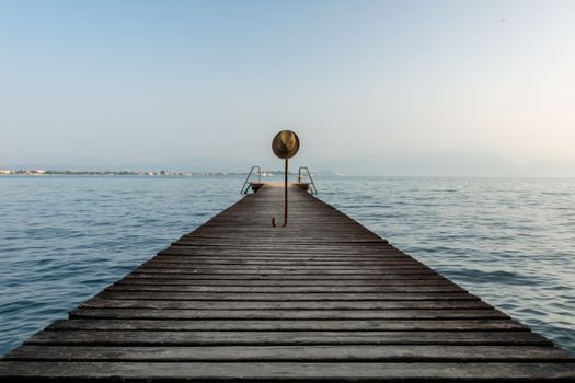 A tranquil wooden pier extending into a calm lake, adorned with a straw hat at sunrise.
