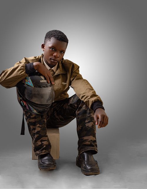 Free Portrait of a young man in camo pants holding a motorcycle helmet, seated with a confident pose. Stock Photo