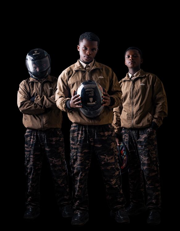 Free Three young go-kart drivers in matching camouflage outfits, holding helmets, amid a dark studio setting. Stock Photo
