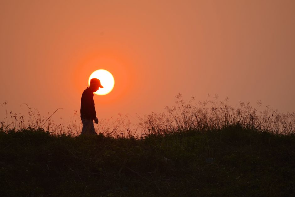 A serene silhouette of a man walking along a grassy hill with the sun setting in Hà Nội, Vietnam.