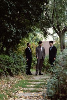 Three businessmen in suits converse on a garden pathway amidst lush greenery.