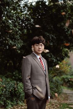 Professional portrait of a man in a striped suit and red tie, standing outdoors with a natural backdrop.