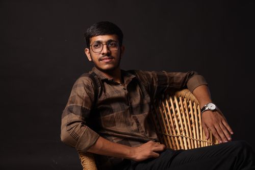 Free Portrait of a young man with glasses, posing confidently on a wicker chair in a studio setting. Stock Photo
