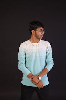 Elegant studio portrait of a young man in glasses, wearing a stylish turquoise sweater, showcasing modern fashion.