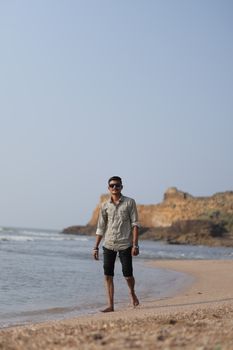 A man enjoys a peaceful walk along a scenic coastal beach with cliffs in the background.