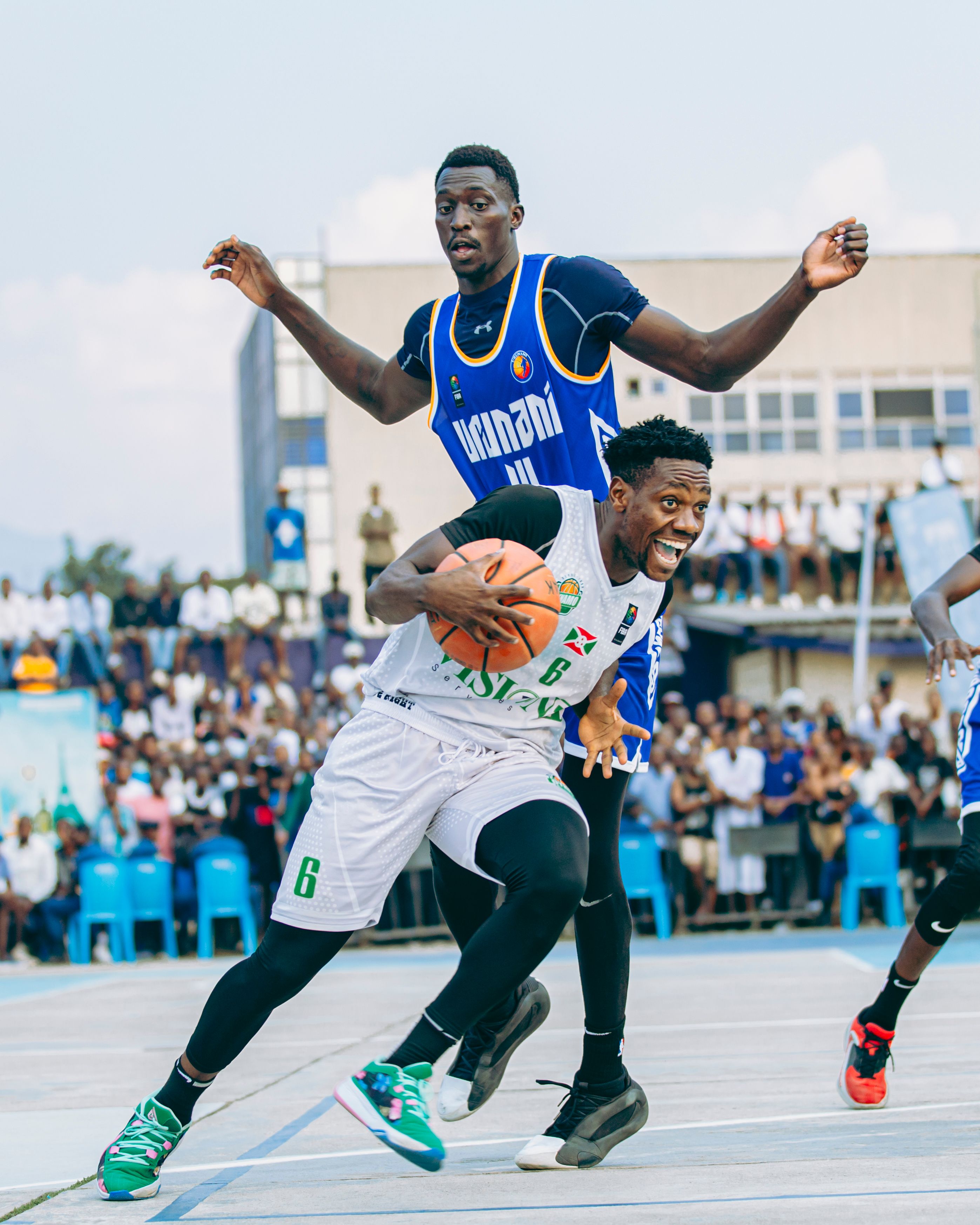 Basketball players in intense outdoor action during a competitive match with spectators.