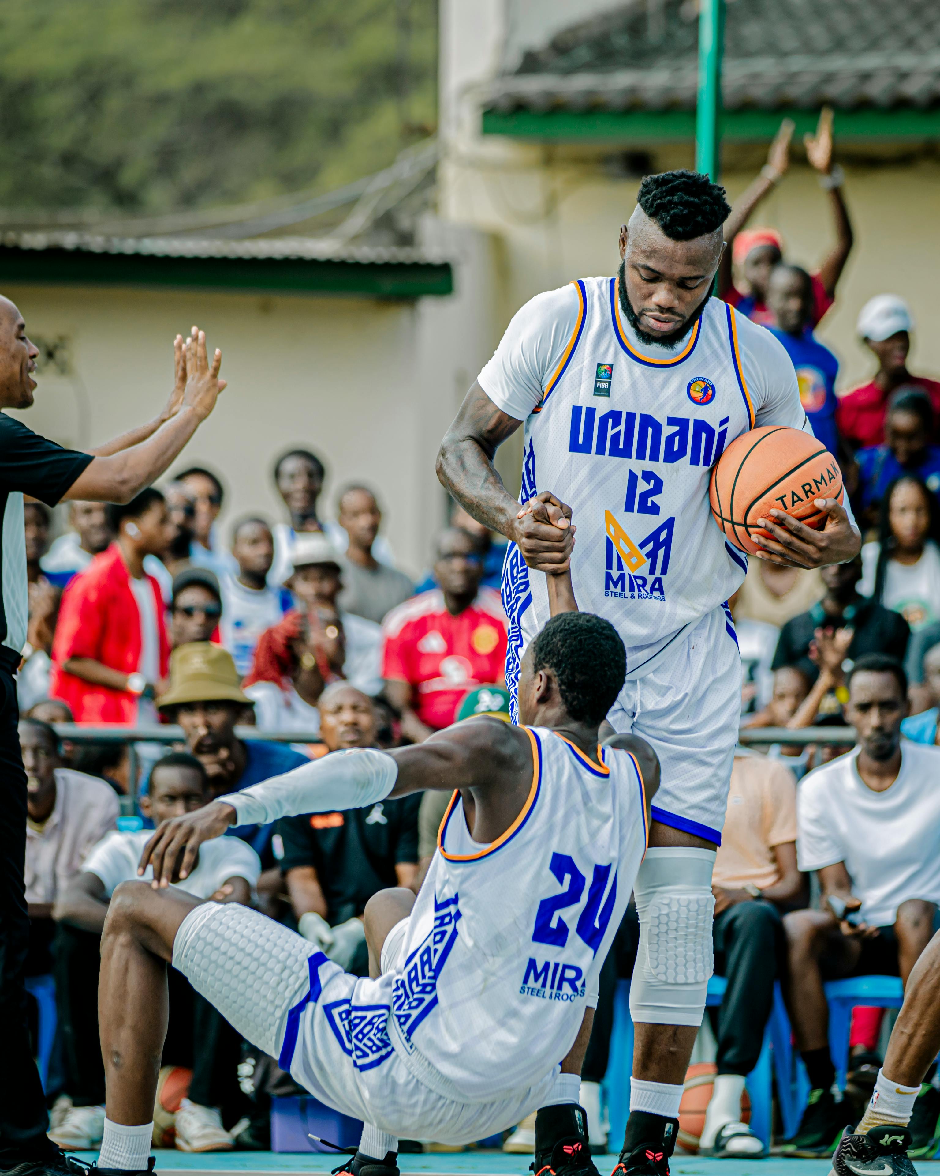 Players compete fiercely in an outdoor basketball game, surrounded by a vibrant crowd.