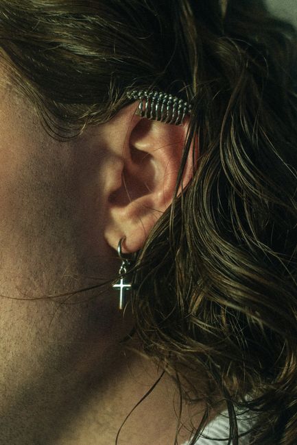 Detailed image of an ear with a cross earring and a metal coil accessory.