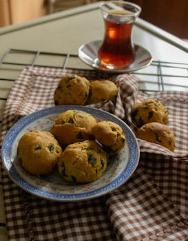 Freshly baked herb-infused rolls served with a glass of tea on a brown checkered cloth.