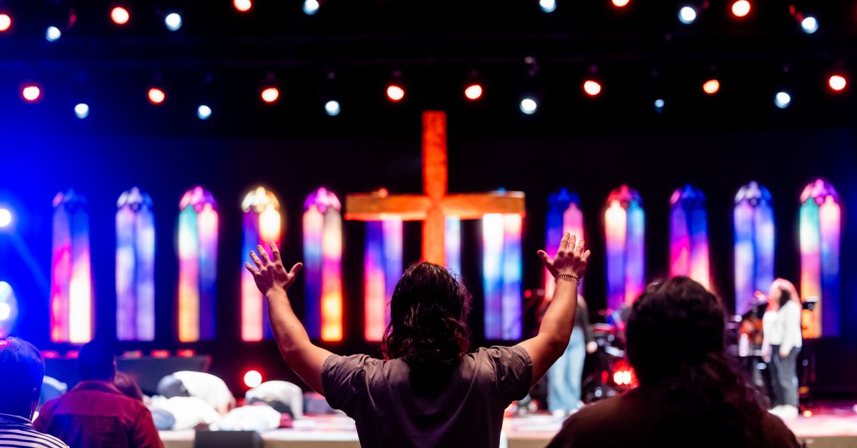 A wide-angle shot of Christ Embassy Loveworld Arena filled with young people in casual clothing, hands raised during worship, with professional stage lighting