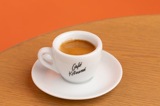 Close-up of espresso served in a Café Kitsuné branded cup on a wooden table.