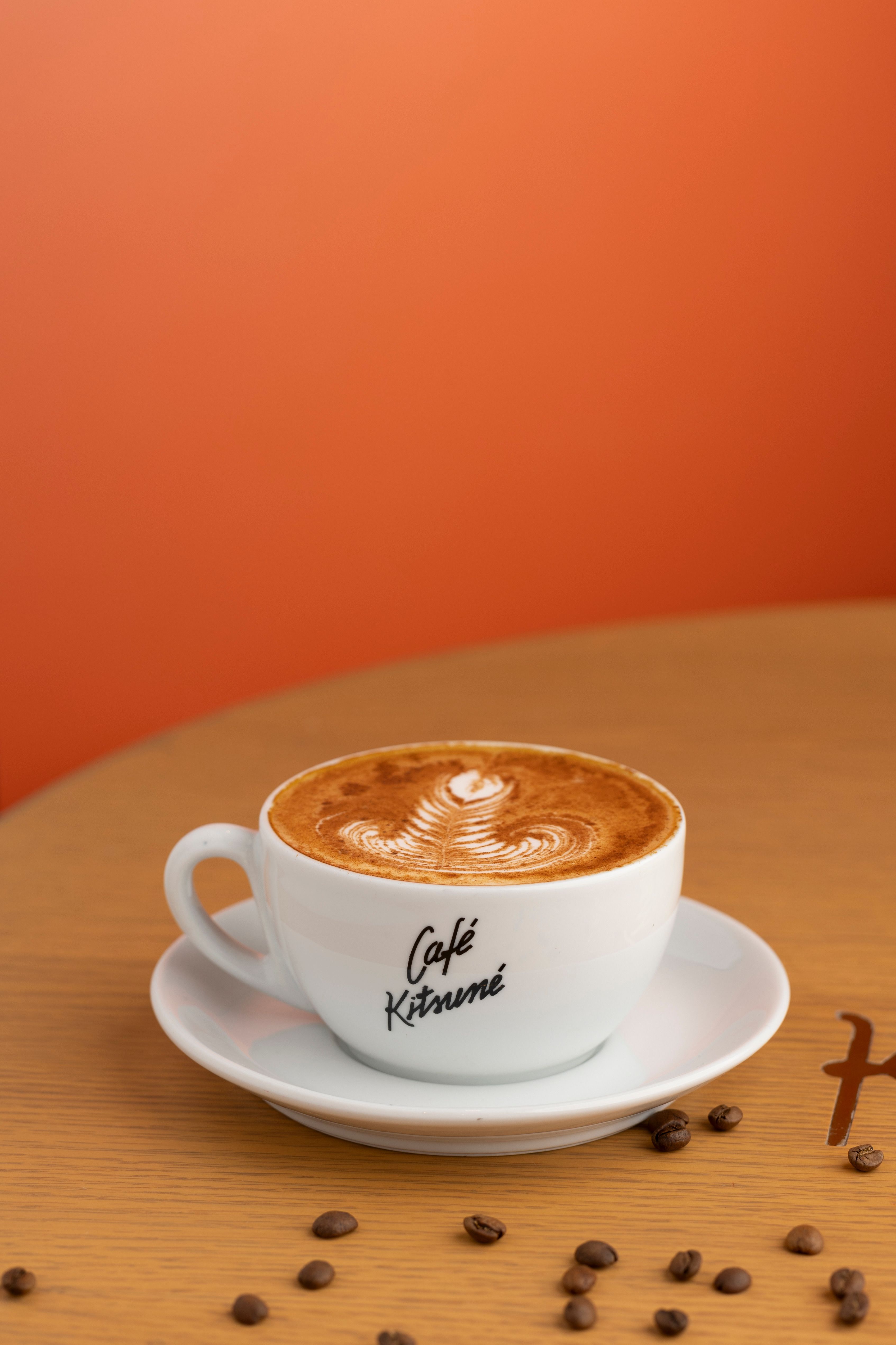 A cup of cappuccino with latte art at Café Kitsuné, set against an orange background.