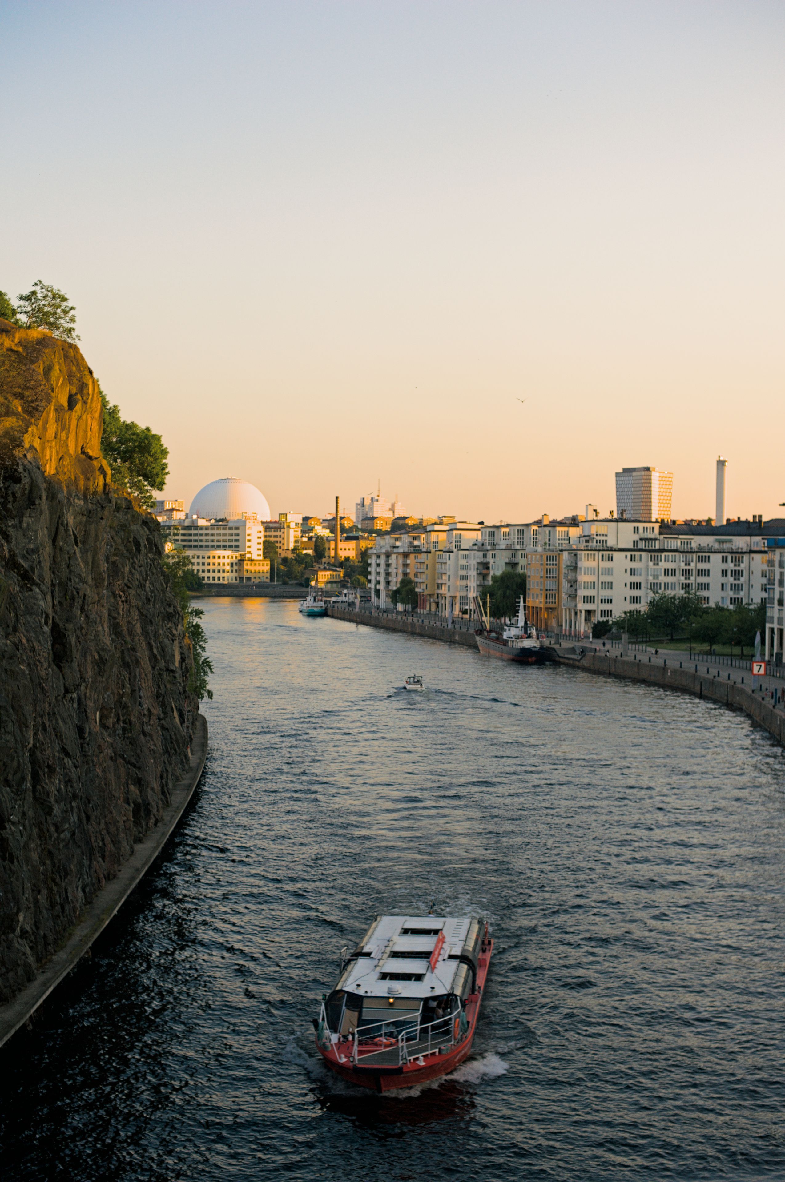 Gratis En pittoresk utsikt over en båt som seiler langs en kanal i Stockholm ved solnedgang. Arkivbilde